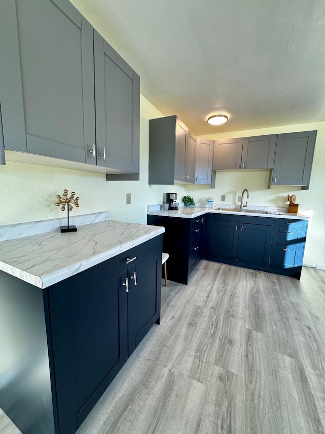 kitchen featuring sink, gray cabinetry, light wood-type flooring, light stone countertops, and a textured ceiling