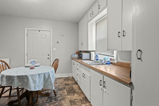 kitchen with white microwave, stone finish floor, a sink, and white cabinets