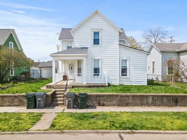 traditional home featuring covered porch, fence, central air condition unit, a front lawn, and roof with shingles