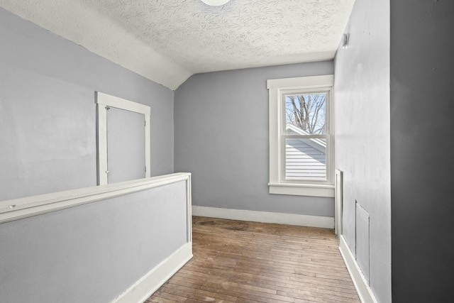 hall with lofted ceiling, hardwood / wood-style floors, baseboards, and a textured ceiling