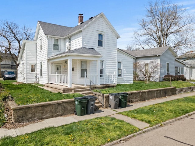 traditional-style home featuring roof with shingles, a chimney, covered porch, and a front lawn