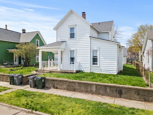 view of front of home featuring a porch, roof with shingles, a chimney, and a front lawn