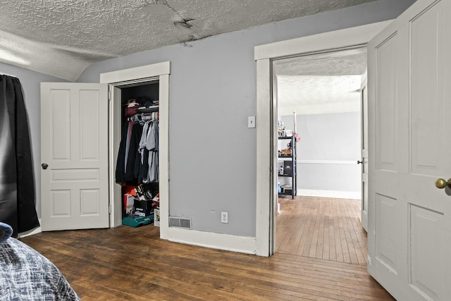 bedroom with a textured ceiling, a closet, a walk in closet, wood-type flooring, and baseboards