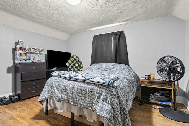 bedroom with baseboards, a textured ceiling, hardwood / wood-style flooring, and lofted ceiling