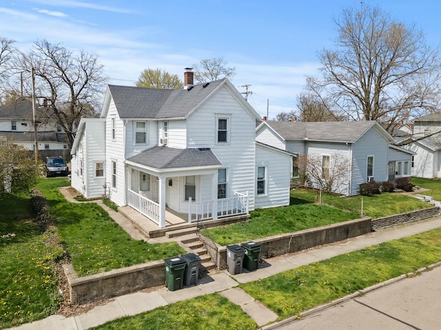 view of front of home with a front yard, a porch, a shingled roof, and a chimney