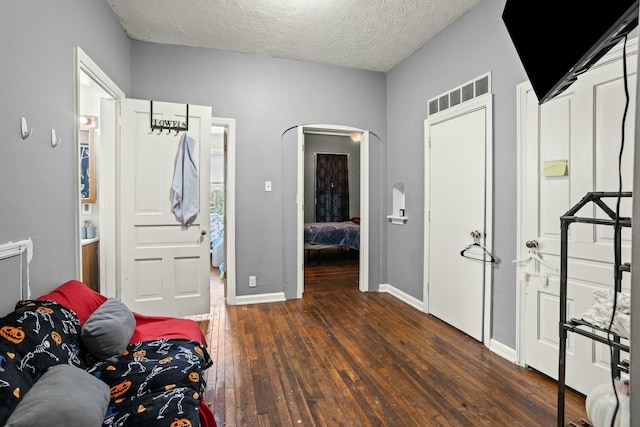 bedroom featuring baseboards, arched walkways, hardwood / wood-style flooring, and a textured ceiling