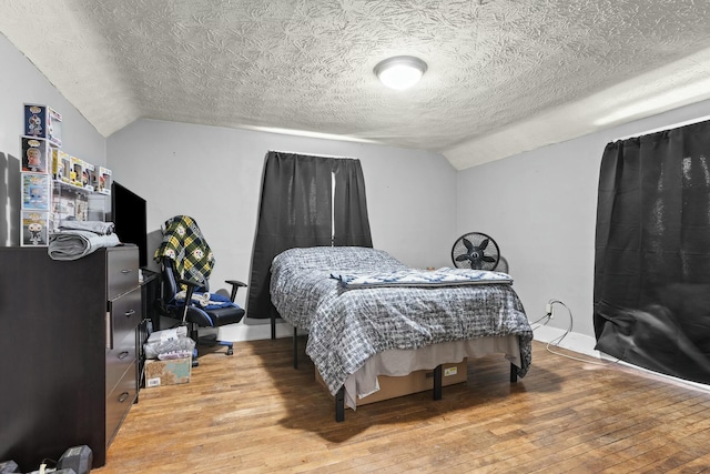 bedroom with light wood finished floors, a textured ceiling, and lofted ceiling