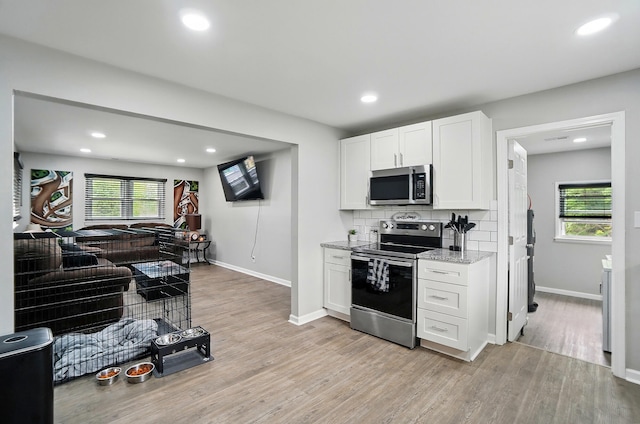 kitchen with appliances with stainless steel finishes, plenty of natural light, light stone countertops, and light wood-type flooring