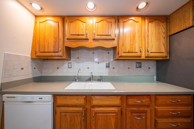 kitchen featuring brown cabinetry, a sink, white dishwasher, light countertops, and backsplash