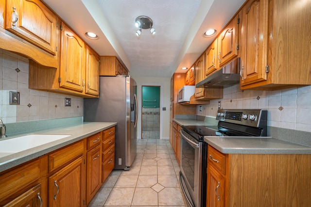 kitchen with appliances with stainless steel finishes, light countertops, brown cabinetry, and under cabinet range hood