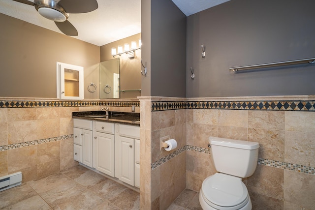 bathroom featuring a wainscoted wall, tile walls, toilet, baseboard heating, and vanity