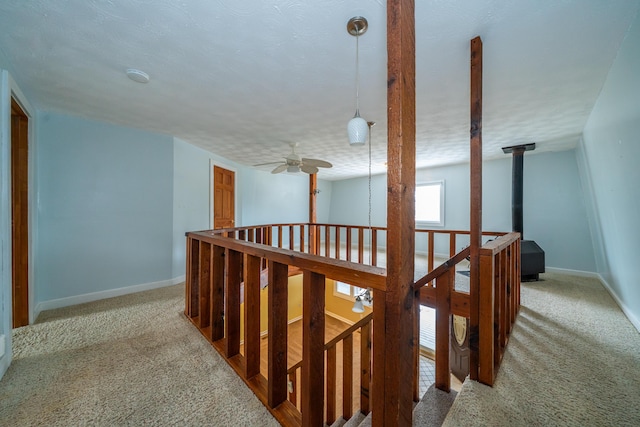 corridor with light carpet, a textured ceiling, an upstairs landing, and baseboards