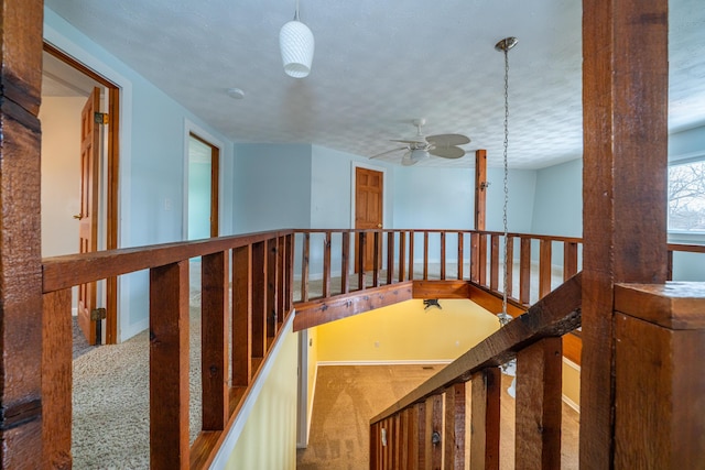 hall featuring carpet floors, baseboards, a textured ceiling, and an upstairs landing