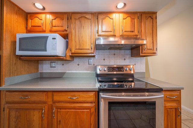 kitchen with under cabinet range hood, brown cabinetry, white microwave, and stainless steel range with electric cooktop