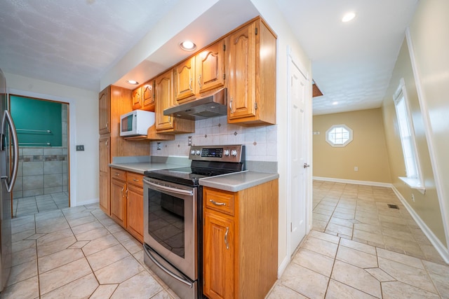 kitchen featuring light countertops, electric range, white microwave, brown cabinetry, and under cabinet range hood