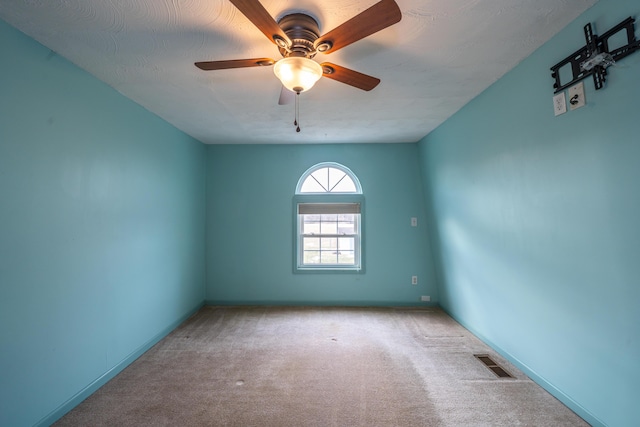 carpeted spare room with baseboards, visible vents, and a ceiling fan