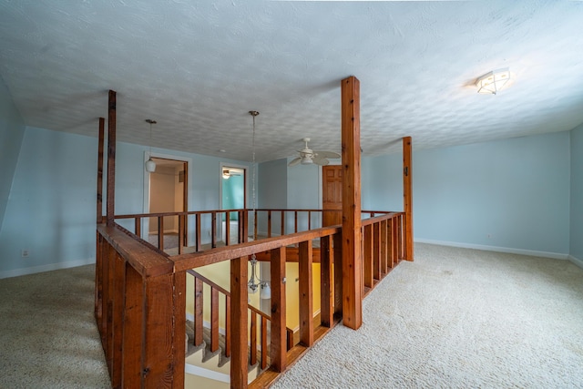 hallway featuring carpet floors, baseboards, a textured ceiling, and an upstairs landing