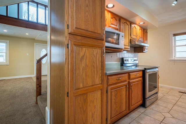 kitchen with brown cabinets, stainless steel electric range oven, backsplash, white microwave, and under cabinet range hood