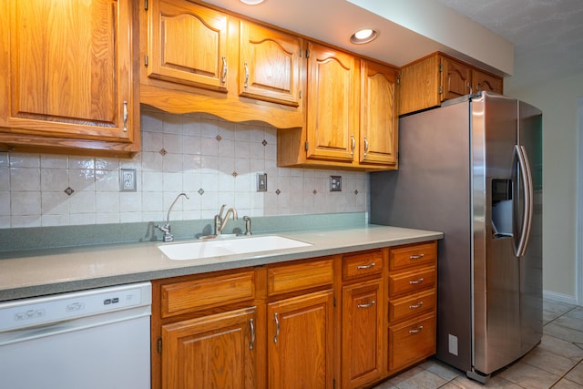 kitchen with brown cabinetry, stainless steel fridge with ice dispenser, white dishwasher, light countertops, and a sink