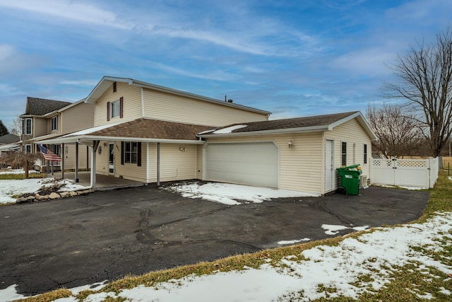 view of snow covered exterior featuring roof with shingles, covered porch, an attached garage, fence, and driveway