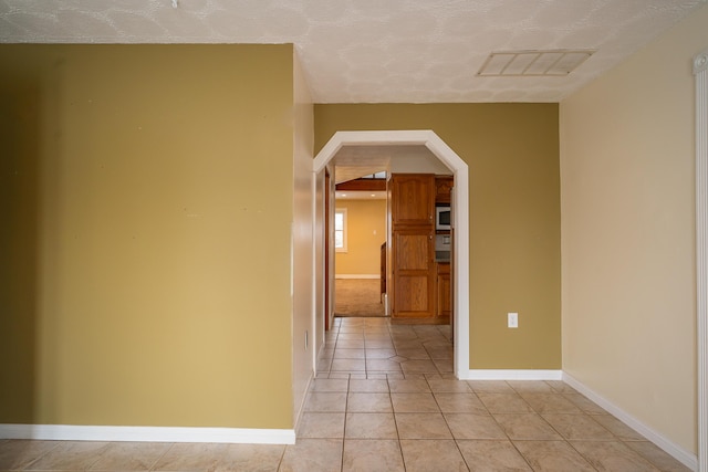 corridor featuring light tile patterned floors, baseboards, visible vents, and arched walkways