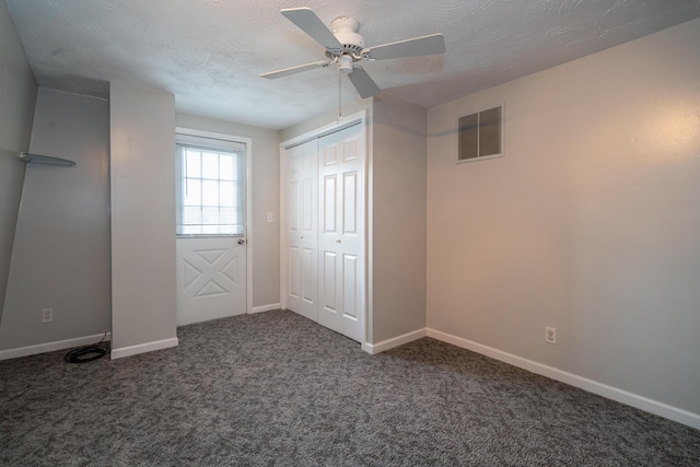 unfurnished bedroom featuring a textured ceiling, dark carpet, visible vents, and baseboards