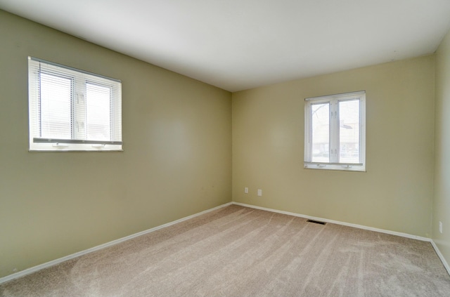 empty room featuring light carpet, visible vents, and baseboards