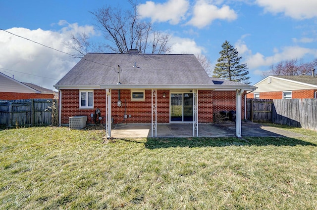 rear view of property with brick siding, a shingled roof, a lawn, a fenced backyard, and a patio area