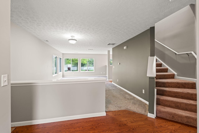 corridor featuring a textured ceiling, visible vents, wood finished floors, stairway, and baseboards