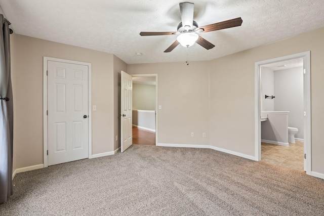 unfurnished bedroom featuring baseboards, ensuite bathroom, ceiling fan, a textured ceiling, and carpet