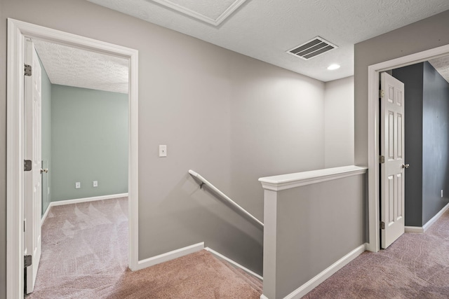 corridor with visible vents, baseboards, a textured ceiling, carpet, and an upstairs landing