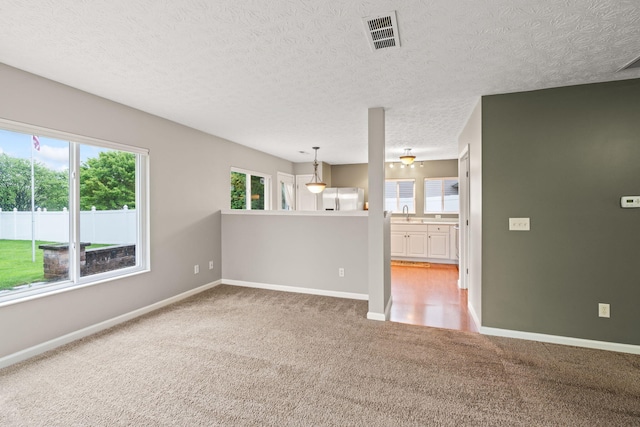 spare room featuring baseboards, light colored carpet, a textured ceiling, and visible vents