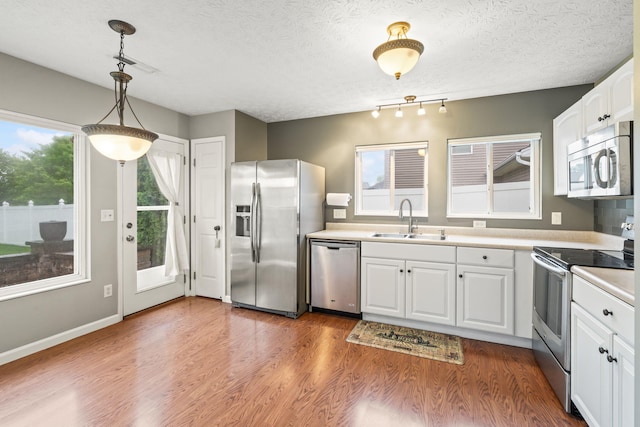 kitchen featuring stainless steel appliances, white cabinetry, a sink, and wood finished floors