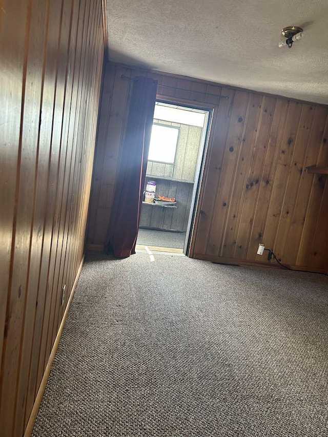 unfurnished room with carpet floors, wood walls, and a textured ceiling