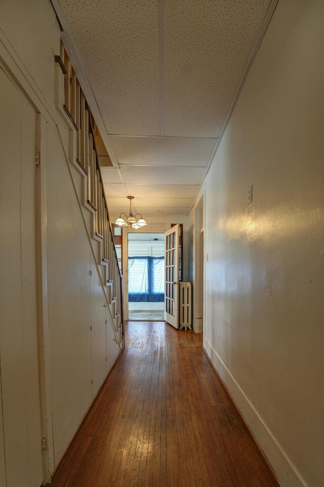 hall with a notable chandelier, radiator heating unit, hardwood / wood-style floors, baseboards, and stairway