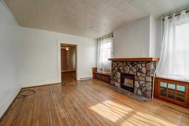 unfurnished living room featuring baseboards, a stone fireplace, ornamental molding, and hardwood / wood-style flooring