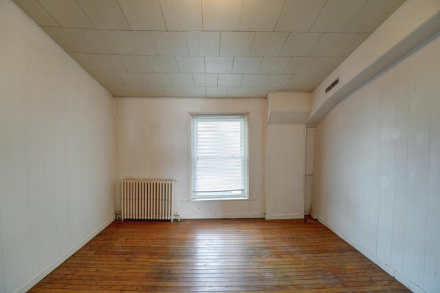spare room featuring wood-type flooring, wood walls, visible vents, and radiator