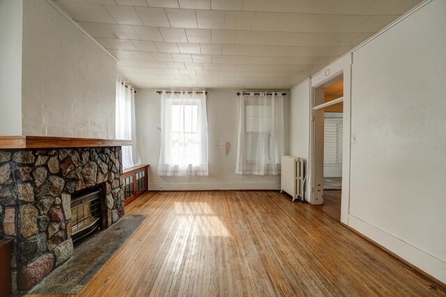 unfurnished living room featuring baseboards, a stone fireplace, radiator heating unit, and hardwood / wood-style floors