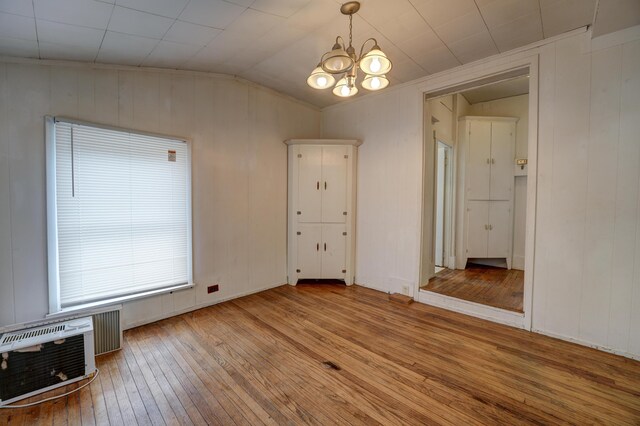 spare room with wooden walls, vaulted ceiling, a notable chandelier, and hardwood / wood-style flooring