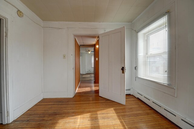 spare room featuring crown molding, attic access, baseboard heating, a baseboard radiator, and light wood-style flooring