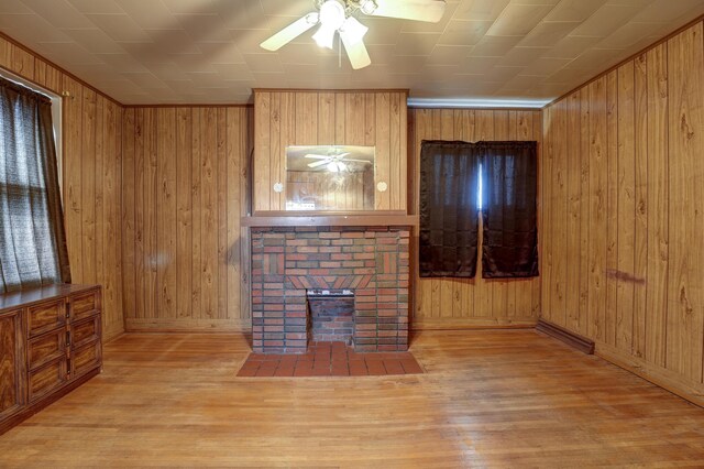unfurnished living room with a brick fireplace, wood walls, a ceiling fan, baseboards, and wood finished floors