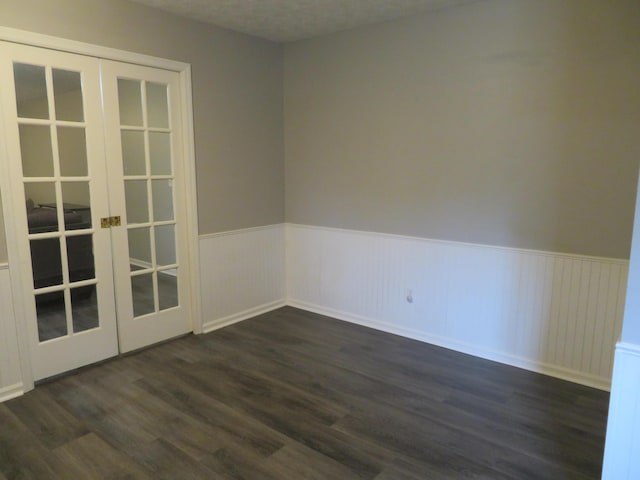 empty room featuring dark wood-style flooring, french doors, and a wainscoted wall
