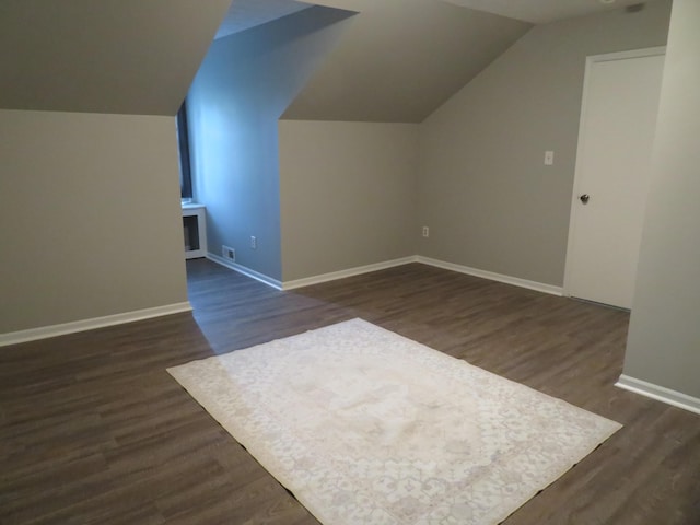 additional living space with baseboards, vaulted ceiling, dark wood-style floors, and visible vents