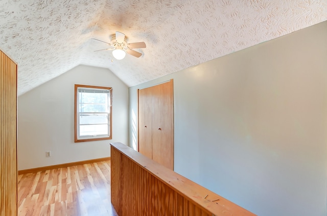 additional living space with ceiling fan, light hardwood / wood-style flooring, a textured ceiling, and vaulted ceiling