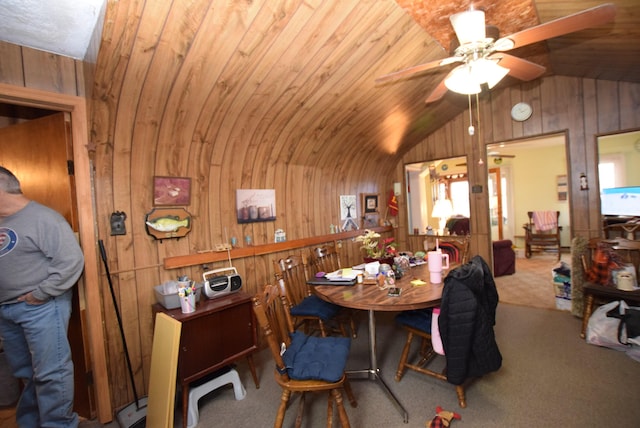 carpeted dining space with lofted ceiling, wood ceiling, wooden walls, and ceiling fan