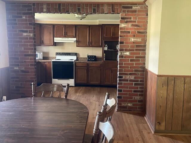 9770 Agerter Rd, Spencerville, OH 45887 - kitchen featuring white electric range, under cabinet range hood, a wainscoted wall, light wood-style floors, and wood walls