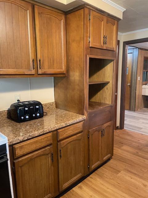 9770 Agerter Rd, Spencerville, OH 45887 - kitchen featuring light wood-style flooring, ornamental molding, brown cabinets, and light stone counters