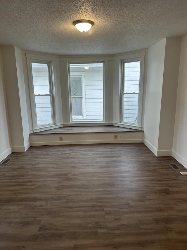 empty room with baseboards, a textured ceiling, visible vents, and dark wood-style flooring