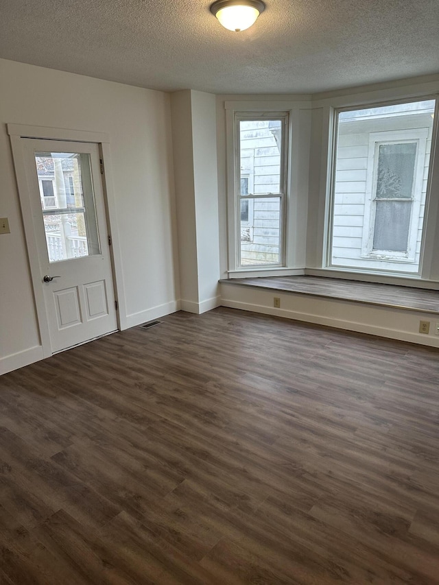 empty room with dark wood-style floors, a textured ceiling, plenty of natural light, and baseboards