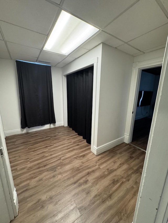 empty room featuring a paneled ceiling, baseboards, and wood finished floors